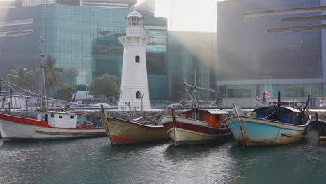 traditional boats docked by a lighthouse in an urban harbor