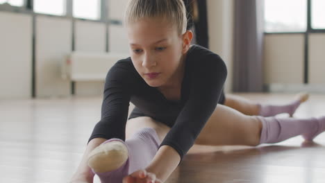 Zwei-Gymnastische-Blonde-Mädchen,-Die-Sich-Die-Beine-Auf-Dem-Boden-Strecken,-Während-Die-Lehrerin-Ihnen-Hilft-1