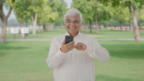 Cheerful-Indian-old-man-scrolling-through-phone-in-park