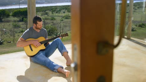 front view of caucasian man playing guitar at porch of beach house 4k