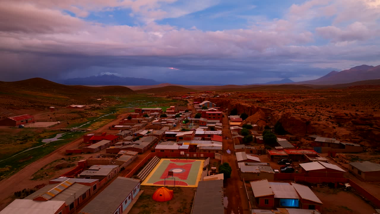 Aguas Calientes, remote town in Bolivian Altiplano, at sunset, vivid sky, desert landscape, and simple buildings, Bolivia. Aerial forward