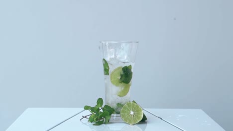 glass with mojito stands on white surface near lime halves