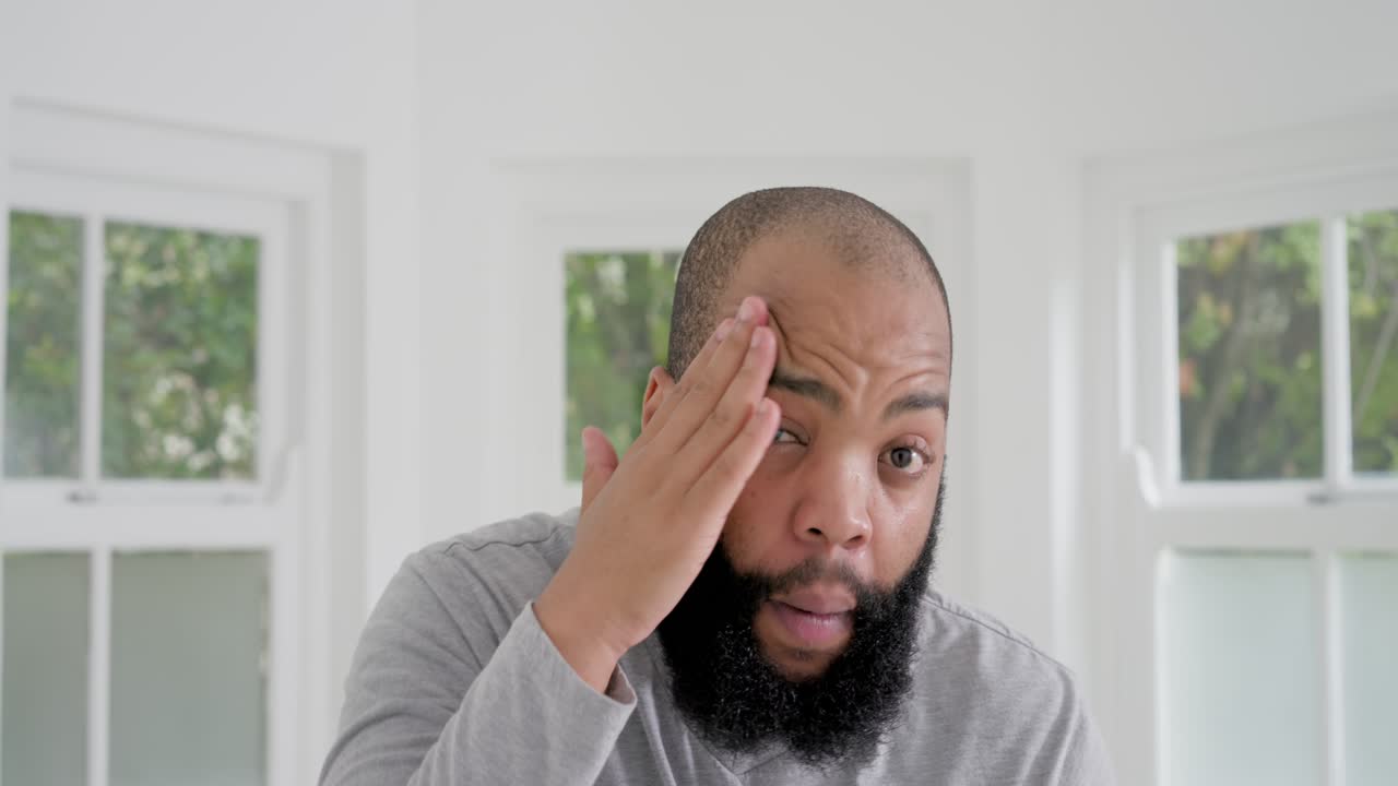 Afroamerikansk mann påfører olje fra ravfarget pipette, gnir skjegget med hendene under hjemmepleie.