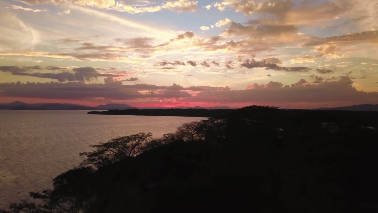 Un atardecer mágico cerca de un lago en Costa Rica, grabado con un dron volando sobre la costa y el bosque.