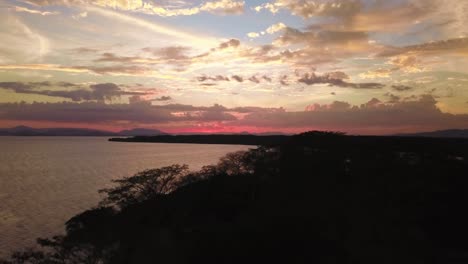 a magical sunset near a lake in costa rica, shot with a drone flying over the coastline and the forest