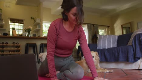 Caucasian-woman-exercising-with-her-pet-dog-using-laptop-at-home
