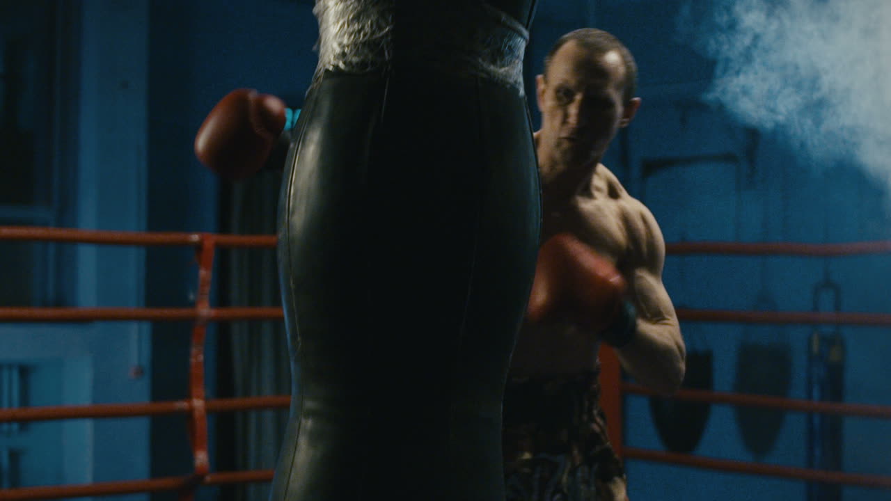 Boxer training with punching bag in boxing ring