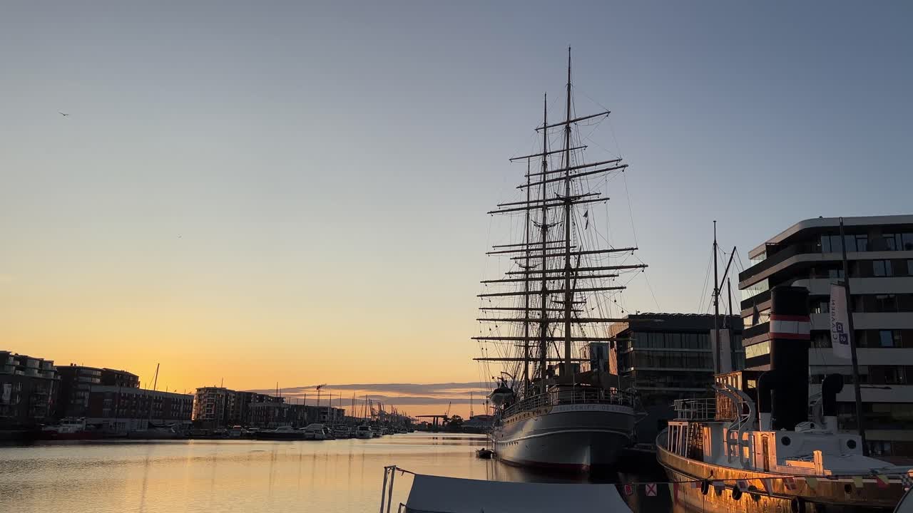 Vista del tramonto sul porto di Bremerhaven con acqua calma, silhouette di storiche navi a vela ed edifici moderni sul lungomare sotto un cielo sereno al crepuscolo