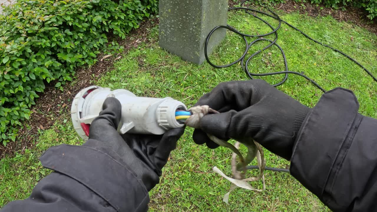Gloved hands hold industrial power cable connector inspecting it for safety outdoors