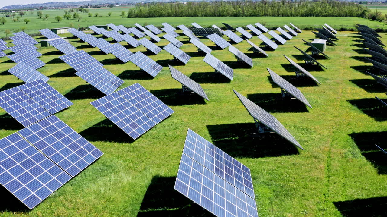 Rows of solar panels on a green field under a clear sky, aerial view