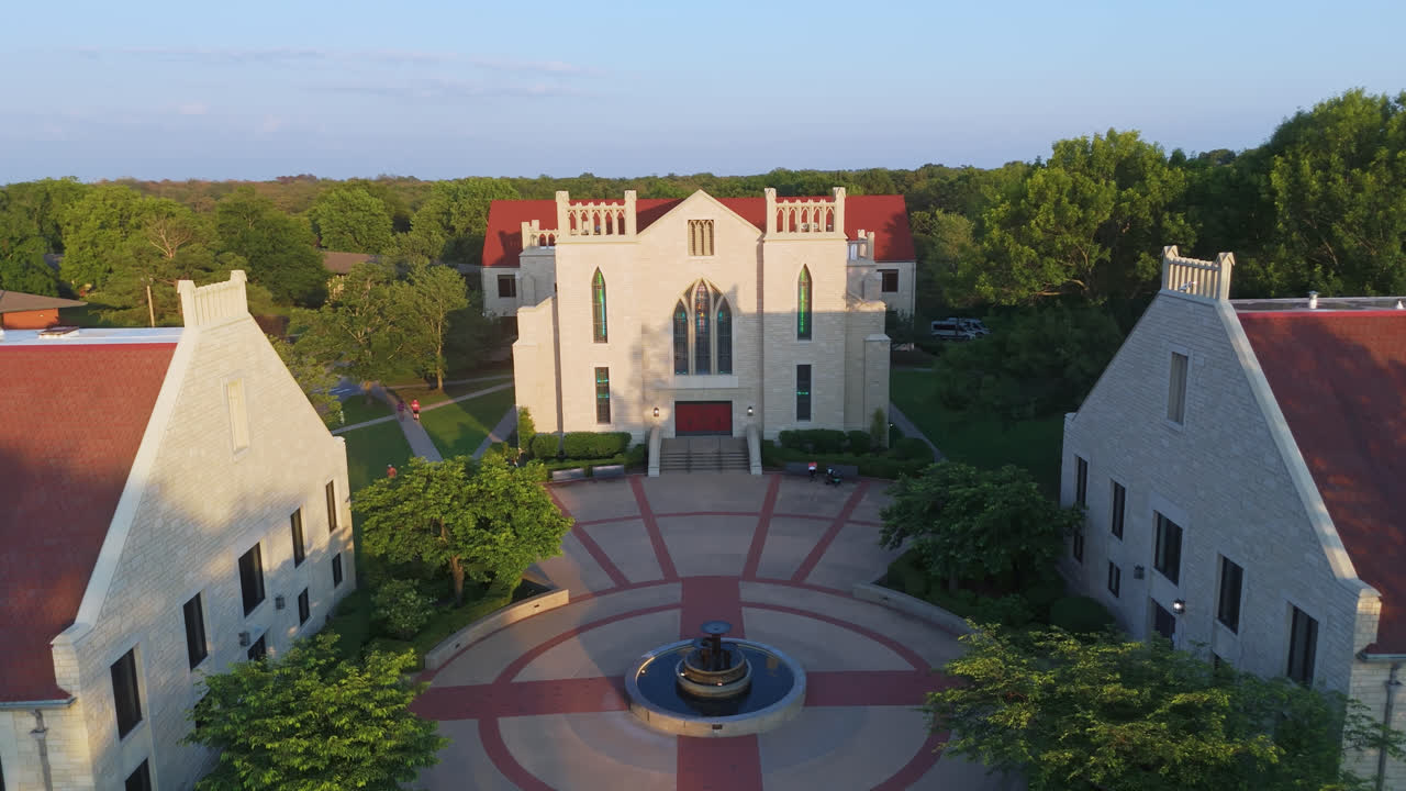 Cattedrale degli Ozarks, edificio accademico in pietra con torre che si eleva sopra gli alberi del campus, ripresa aerea all'indietro.