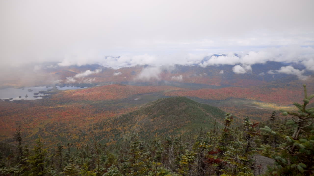una épica vista otoñal de las montañas adirondack con nubes colgantes bajas y hojas rojas y amarillas vibrantes, movimiento panorámico lento