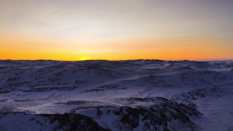 aerial drone footage of a sunset or a sunrise in norwegian mountains that are covered in white ice and snow during winter. drone slowly rises up revealing the orange vibrant sky and sun even more