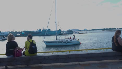 women relaxing by the harbor with sailboats and warships