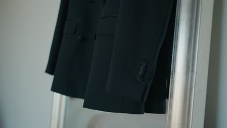 black wedding suit jacket hanging neatly indoors with daylight softly illuminating the fabric