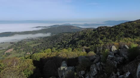 Drone-flying-over-granite-rocks-of-Uchon-with-valley-shrouded-in-fog-in-background,-Morvan-in-France