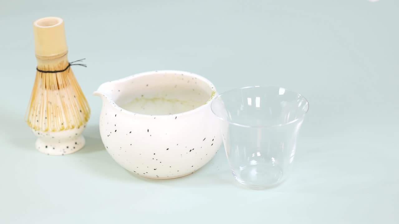 抹茶碗と竹製の茶筅の横にあるグラスに、手で氷を入れている様子。明るいスタジオ照明。
