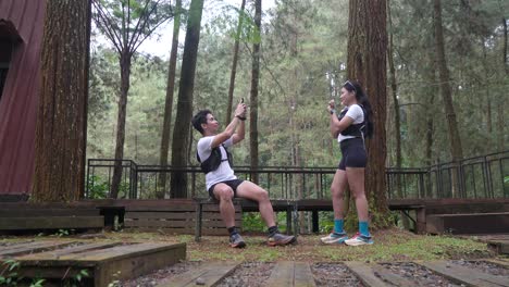asian couple taking photo with smartphone during outdoor trail run in indonesian forest