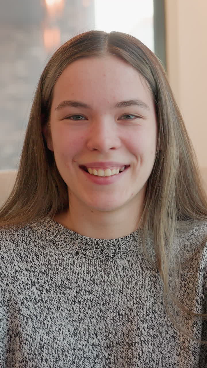 Smiling caucasian woman indoors facing camera, wearing patterned sweater by window with soft natural light warm candid expressions, gentle head tilts and open smile convey friendly approachable mood