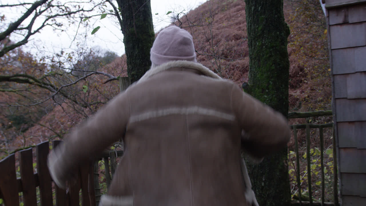 코트를 입고 나무 위의 자연 다리를 건너는 여성