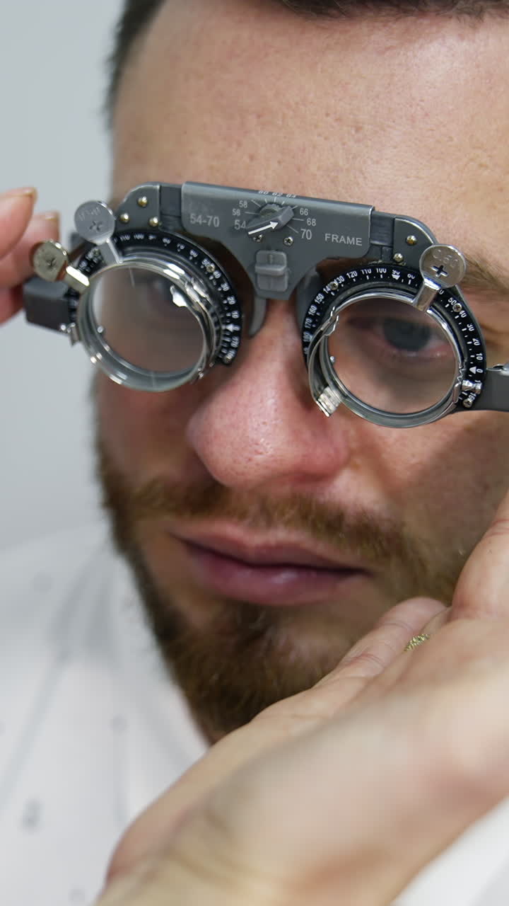 Doctor checks man's sight with optical trial frame. Portrait of a young male patient testing his eyesight in ophthalmological center. Vertical video