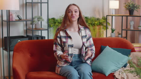 woman sitting on home sofa, looking at camera, making video conference call with friends or parents