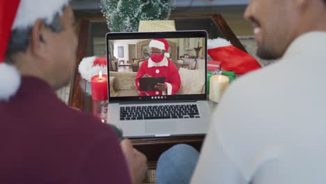 Smiling-biracial-father-and-son-using-laptop-for-christmas-video-call-with-santa-on-screen