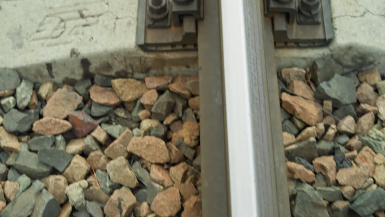 철도 트랙의 고정 시스템의 클로즈업 뷰, 비디오는 비석 돌로 둘러싸인 콘크리트 슬리퍼에 철도를 고정시키는 볼트와 견과류를 강조합니다.