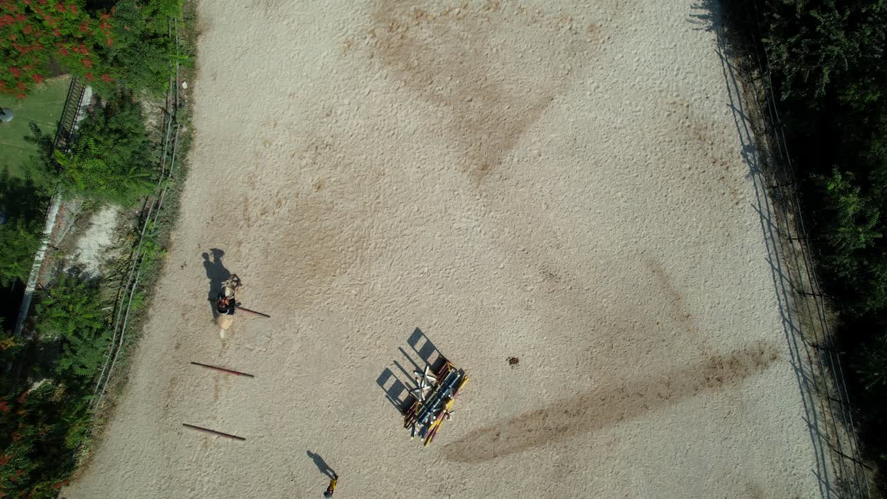 Aerial angle captures a rider appearing quickly and executing jumps between three ground bars with trainer watching