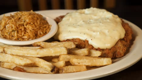 Gebratenes-Hühnchensteak,-Erstickt-In-Gepfefferter-Landsoße-Mit-Schmutzigem-Reis-Und-Pommes-Frites,-Schieberegler-In-Nahaufnahme,-4K