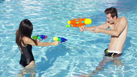 Pareja-Feliz-Disparando-Pistolas-De-Agua-En-La-Piscina