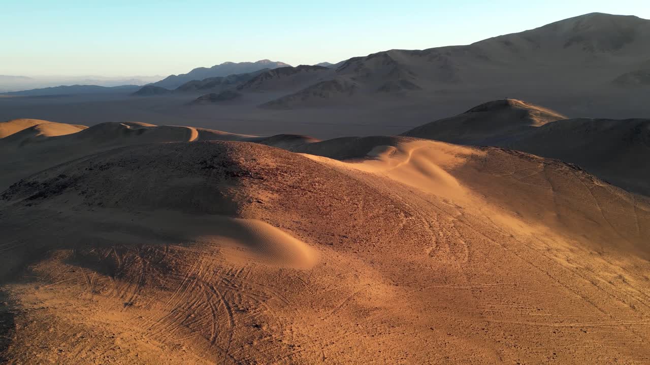 Cinematic drone footage gliding over textured desert dunes, with rippled patterns highlighted by the low sun