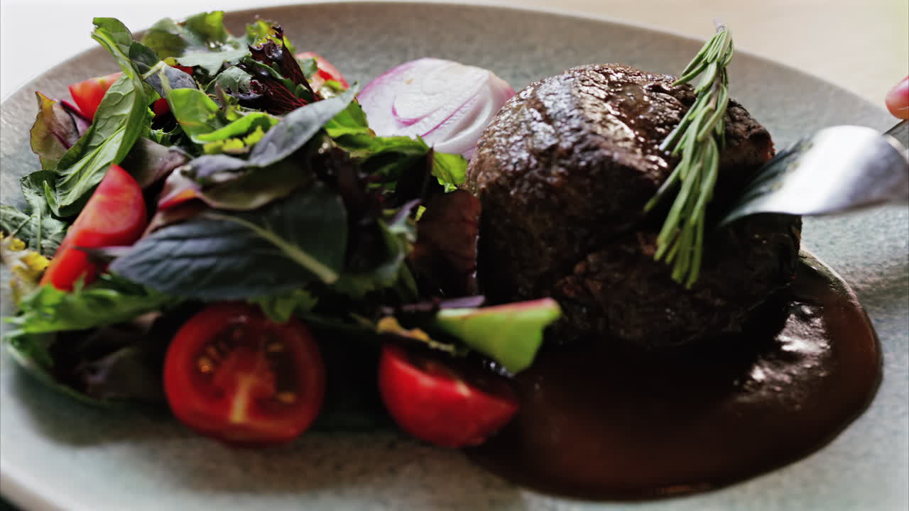 Close up of a filet mignon with a red wine sauce and a fresh salad garnish