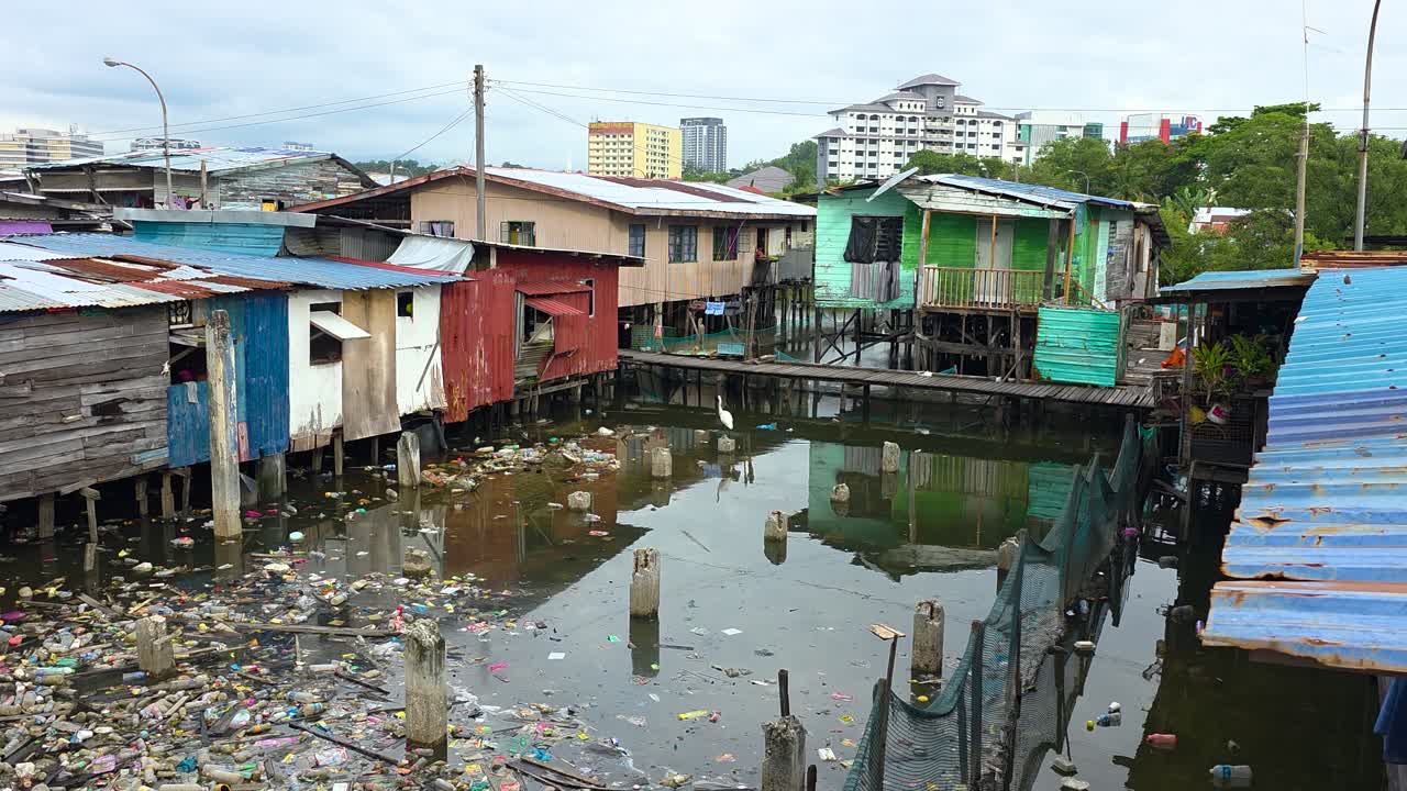 A village of colorful stilt houses built over water in Kota Kinabalu, Malaysia, surrounded by floating plastic trash, highlighting pollution and urban impact