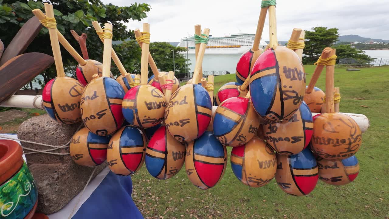 Primo piano di maracas tradizionali fatte a mano in vendita come souvenir, con una grande nave da crociera sullo sfondo a Puerto Plata, Repubblica Dominicana.