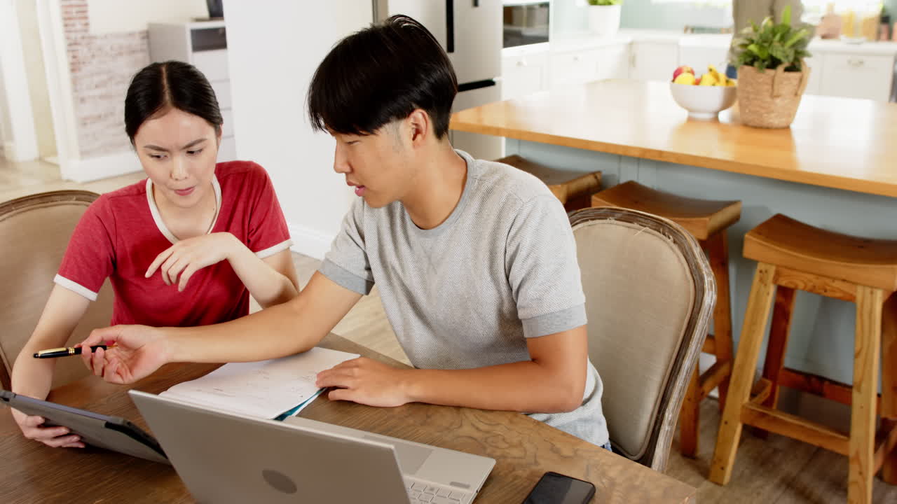 Working from home, couple using laptop and tablet while discussing documents