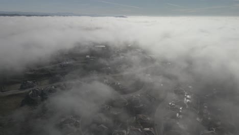 Wide-angle-drone-footage-through-the-cloud-line-on-a-bright-sunny-morning-over-Folsom,-USA-with-scattered-fog-and-mountains-in-the-background
