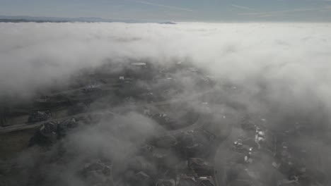 wide angle drone footage through the cloud line on a bright sunny morning over folsom, usa with scattered fog and mountains in the background