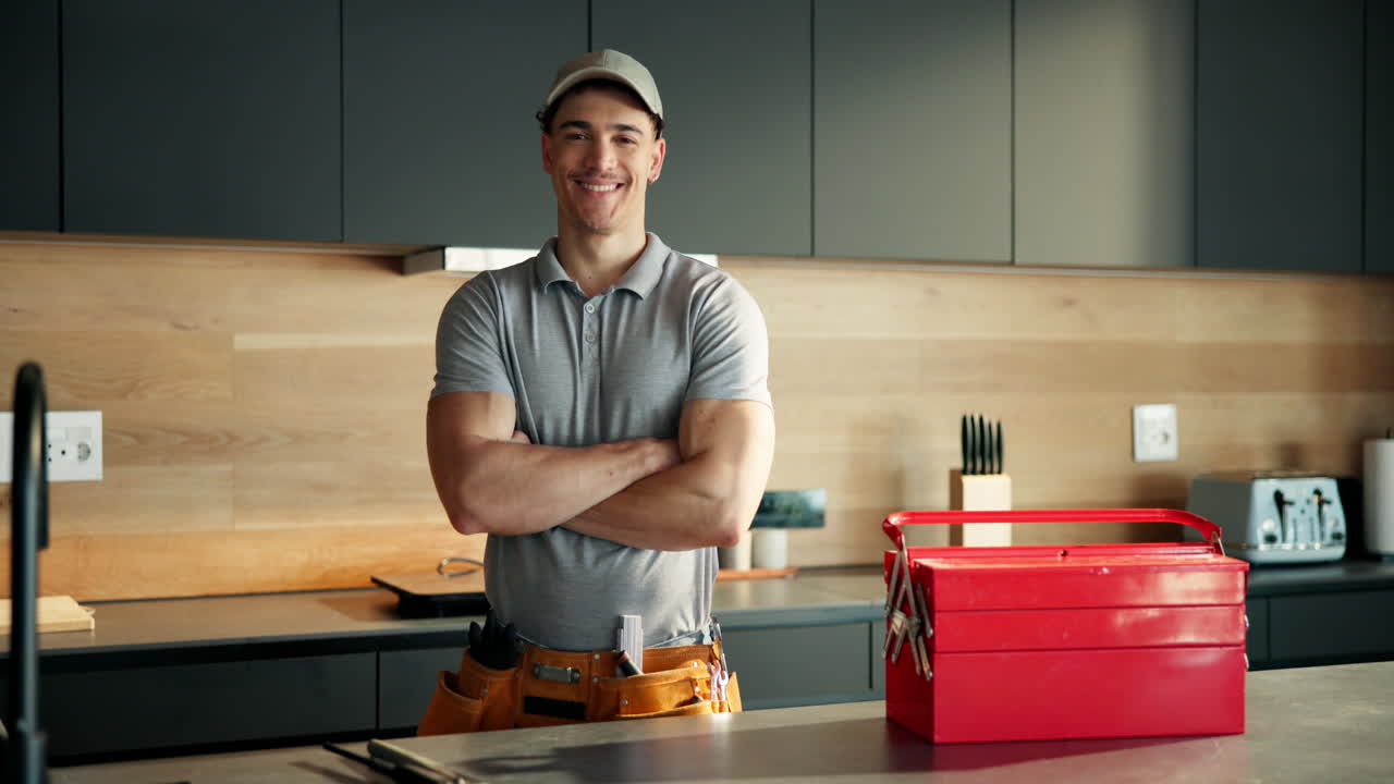 Joven manitas seguro de sí mismo posando con caja de herramientas en cocina moderna