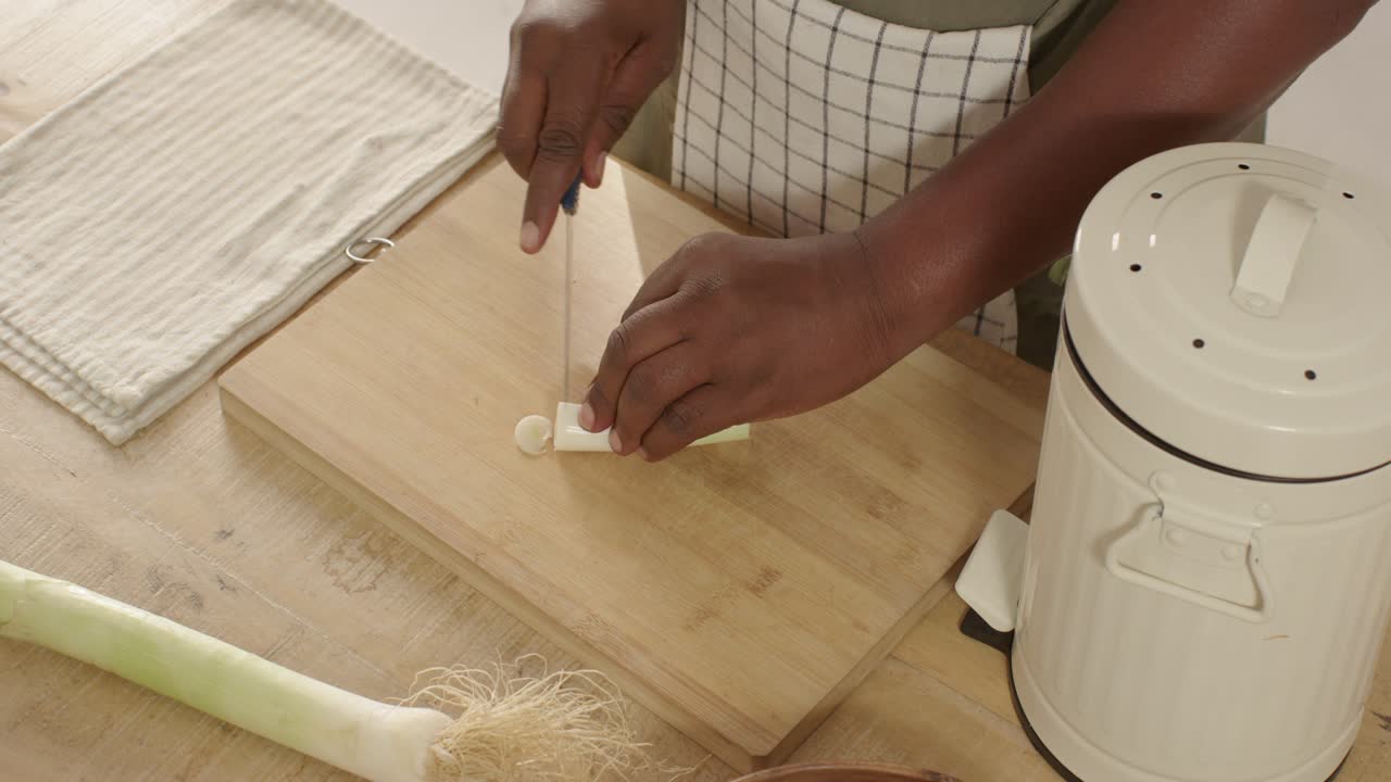 Afrikanischer Koch schneidet Lauchspitzen in den Kompost, zerteilt den Stiel mit einem Messer auf einem Brett, mit Freiraum für Text.
