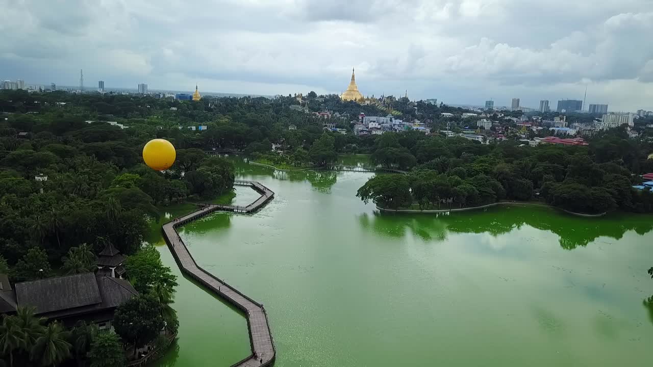 A stunning rising aerial shot over Kandawgyi Lake in Yangon, Myanmar, revealing the vibrant city and the iconic Shwedagon Pagoda in the distance. Perfect for showcasing the city's beauty and landmarks