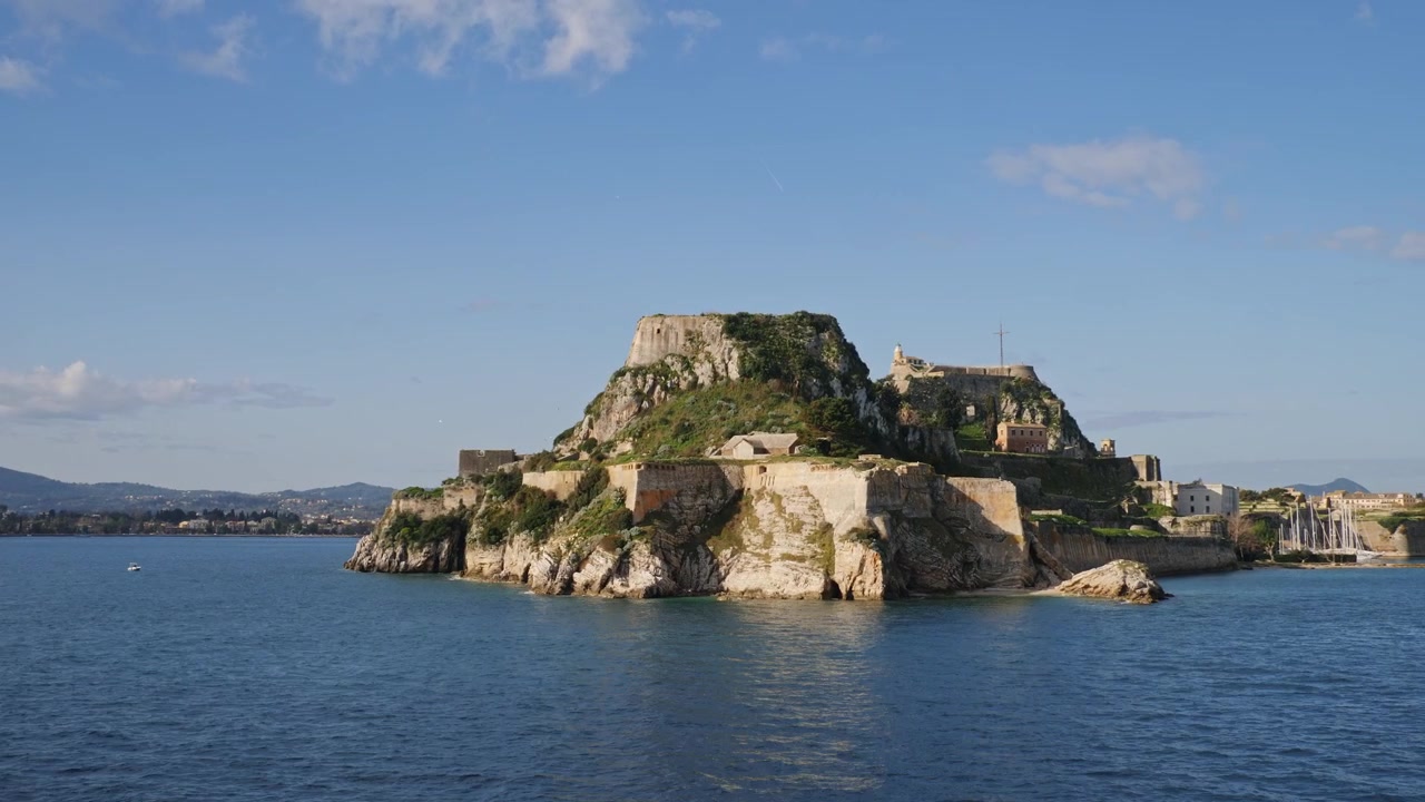 Vista statica dal mare della Vecchia Fortezza Veneziana Palaio Frourio, arroccata su una penisola rocciosa con il faro e il cielo blu, nella città di Corfù, Isole Ionie, Grecia.