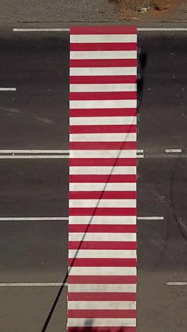 trucks are driving on the highway with a pedestrian crossing in red and white colours. aerial view vertical video