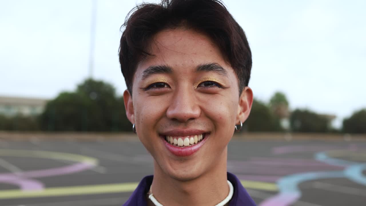 Happy gay chinese man with make-up smiling on camera outdoor