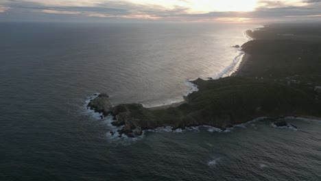 Hazy-ocean-aerial-orbits-rocky-headland-on-coast-of-Mazunte,-Mexico