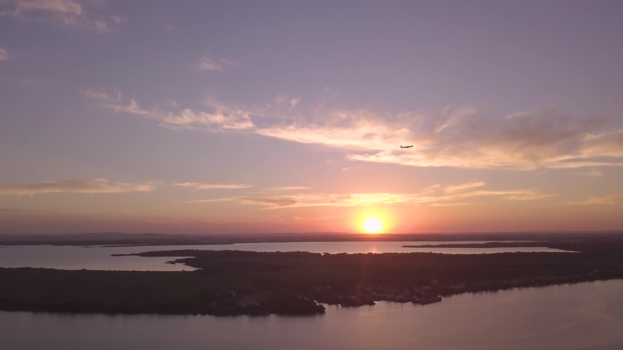 Incroyable prise de vue aérienne 4K d'un avion traversant un ciel pourpre au coucher du soleil au-dessus d'un fleuve au Brésil