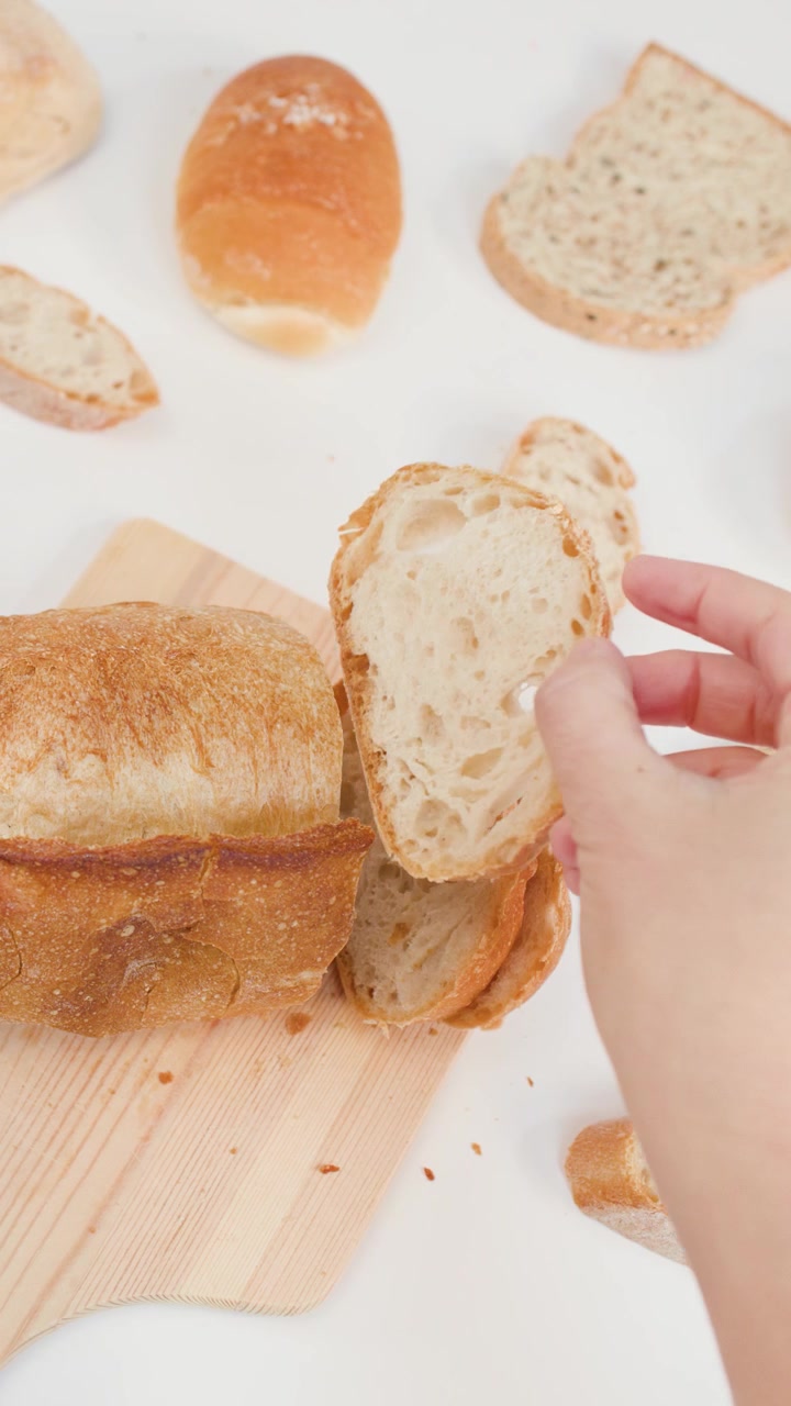 Top-down view of hands selecting a fresh sourdough slice from a wooden cutting board.