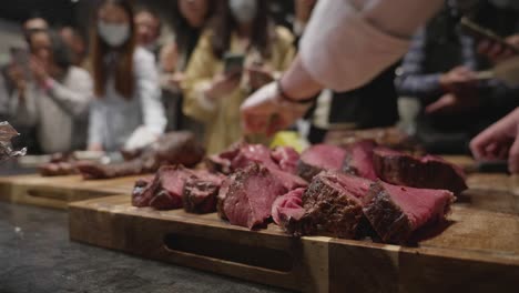 chef puts freshly grilled meat slices together on wooden cut board at meat tasting event