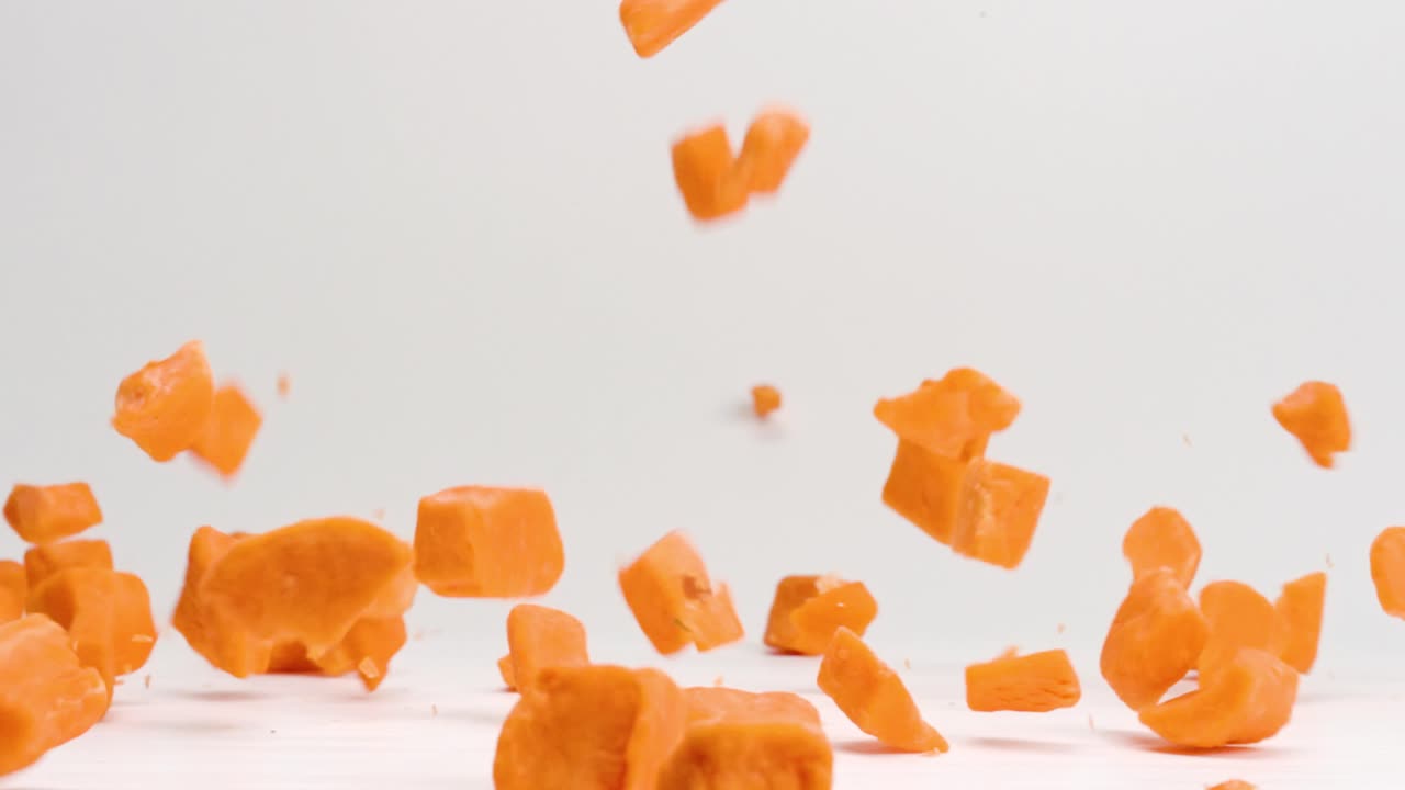 trozos de batata en cubos de color naranja brillante que caen y rebotan sobre la mesa blanca en cámara lenta