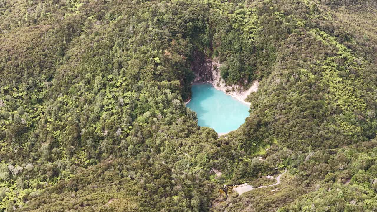 Filmatisk luftfotoinnramming av en skjult blå kratersjø i tett grønn skog, ideelt for reise-, natur- og dokumentarfortellinger.